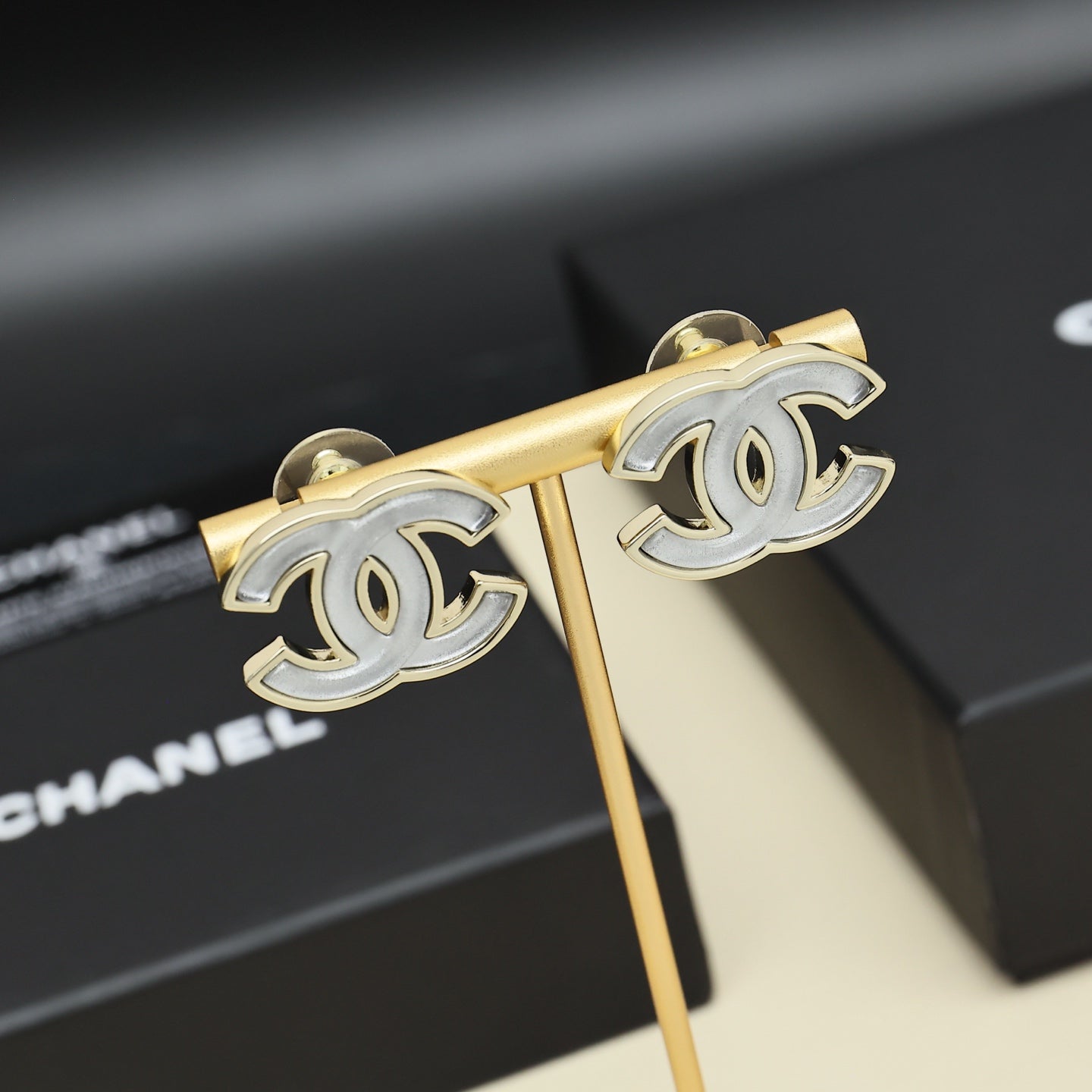 Chanel CC logo earrings on gold-tone display stand, with white enamel details