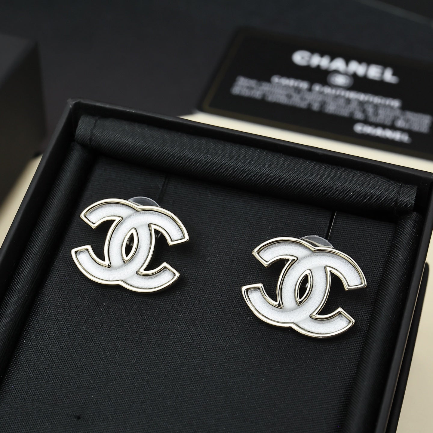 Chanel CC logo stud earrings, silver-tone with white enamel, on black fabric pad