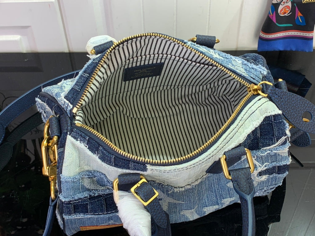 Open blue denim bag showing striped lining and gold zipper trim.