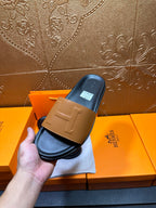 Hermes slide sandals held: tan front strap and dark blue-black footbed on box