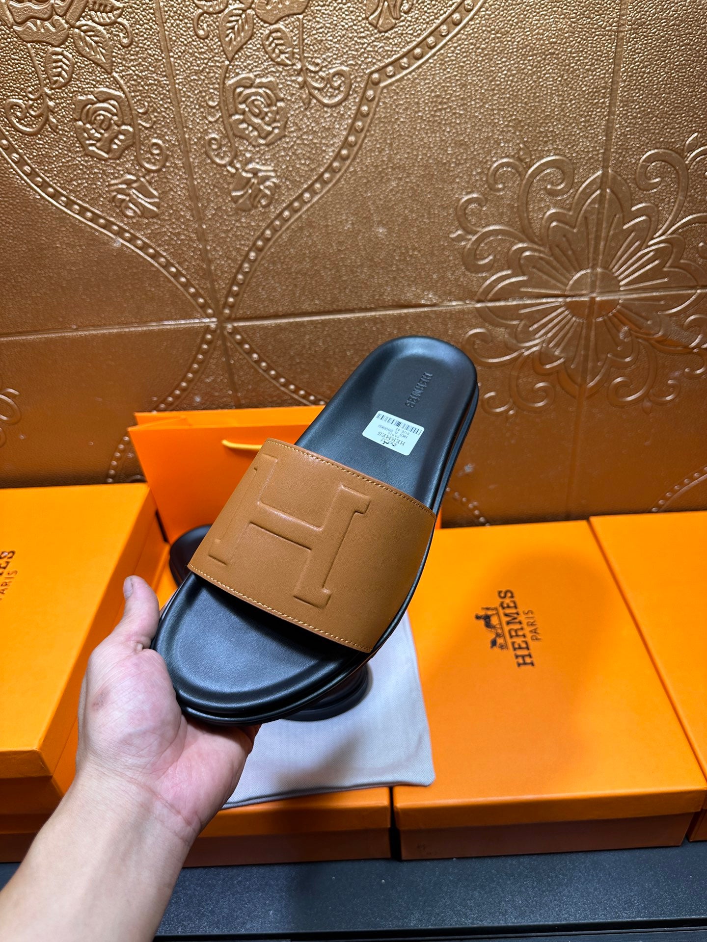 Hermes slide sandals held: tan front strap and dark blue-black footbed on box