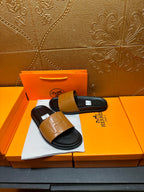 Hermes slide sandals with tan leather band and black footbed, side view on box