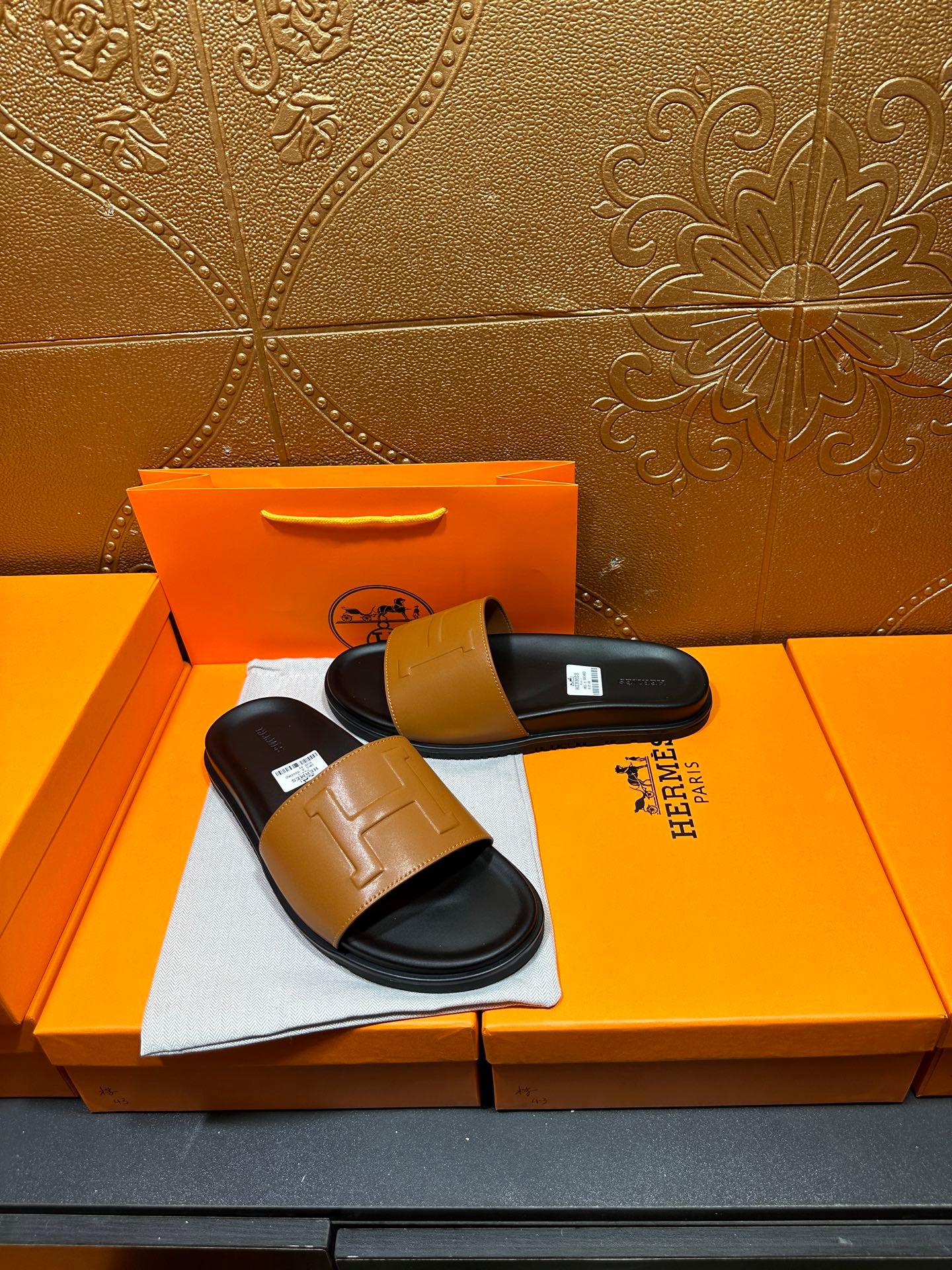 Hermes slide sandals with tan leather band and black footbed, side view on box