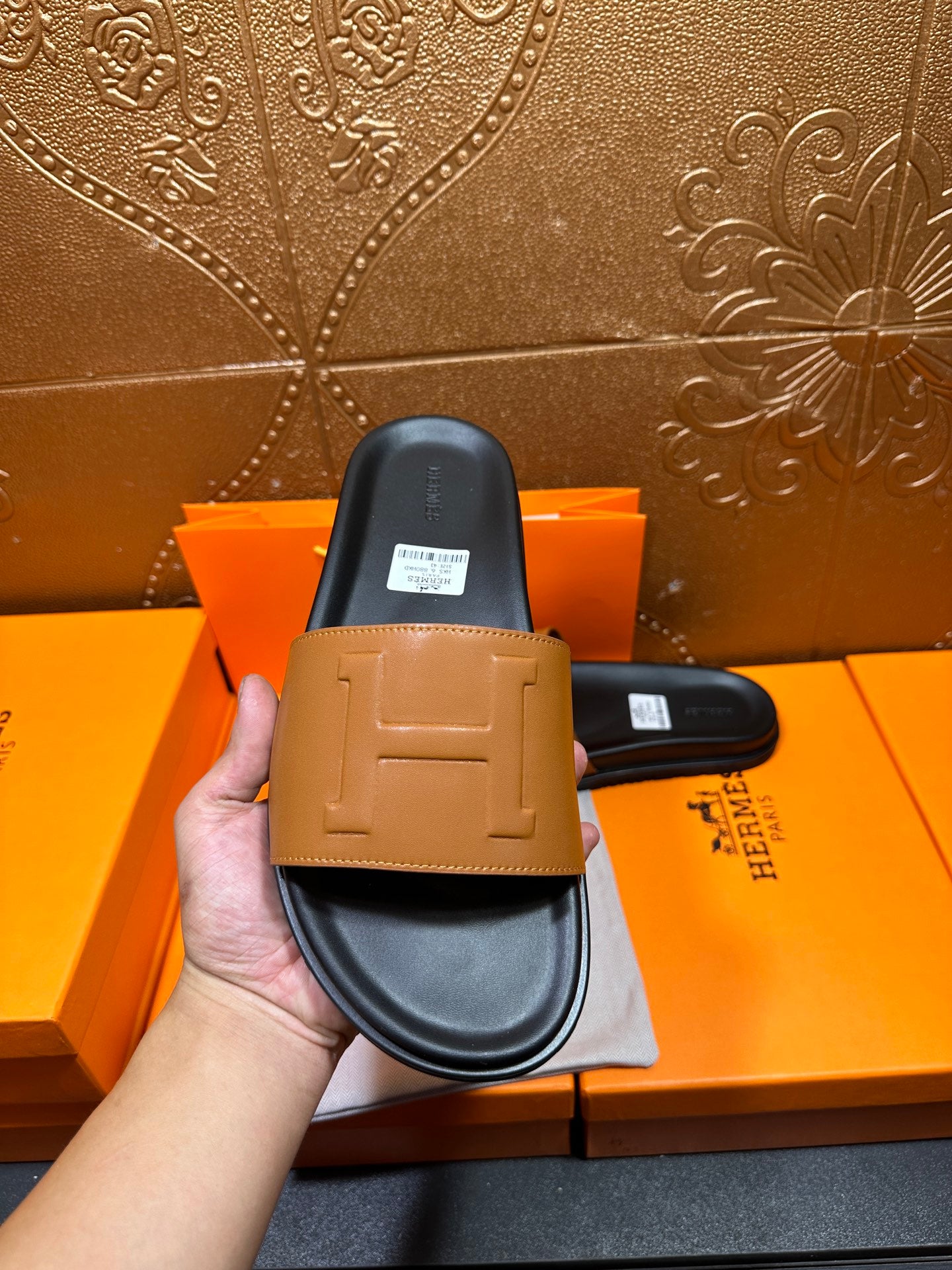 Hermes slide sandals held up: tan strap with embossed detail on black sole