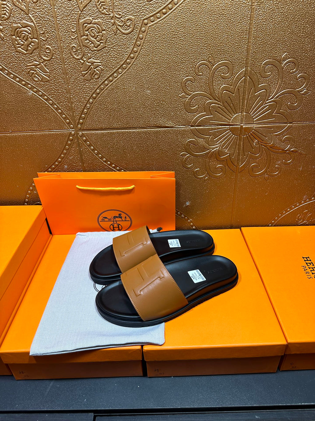 Hermes slide sandals, tan logo strap over dark footbed, shown on orange box