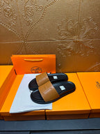 Hermes slide sandals, tan logo strap over dark footbed, shown on orange box