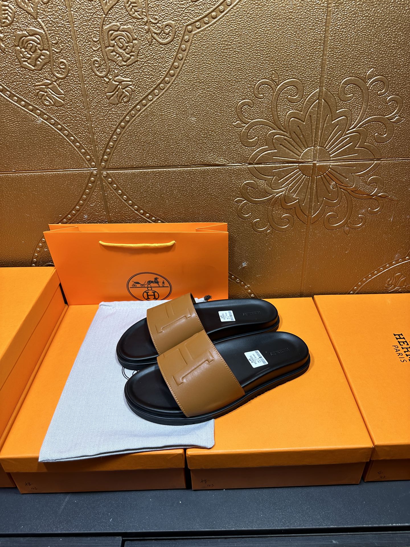 Hermes slide sandals, tan logo strap over dark footbed, shown on orange box
