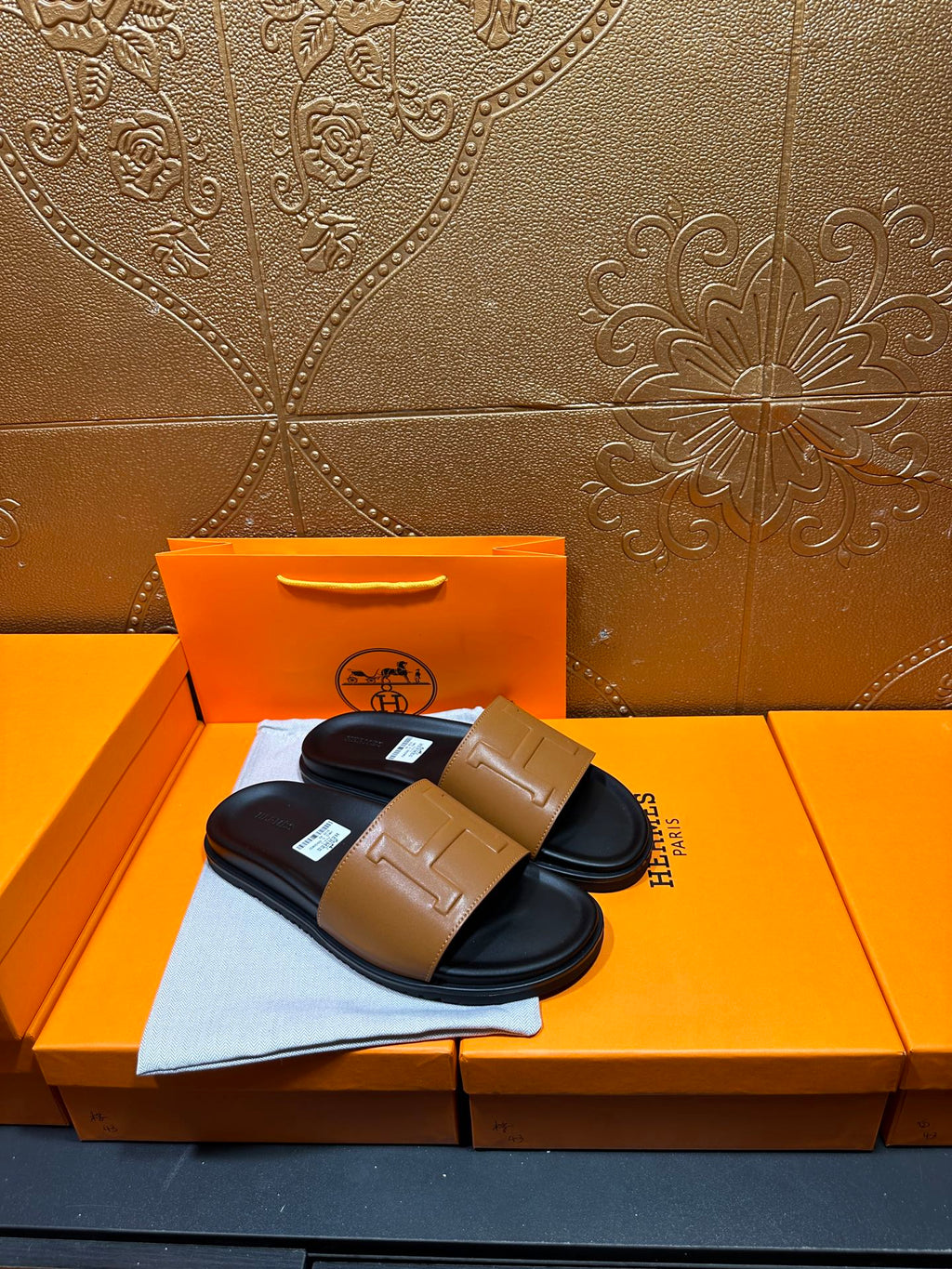 Hermes slide sandals with tan front strap and black sole, pair displayed on box