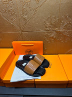 Hermes slide sandals with tan front strap and black sole, pair displayed on box