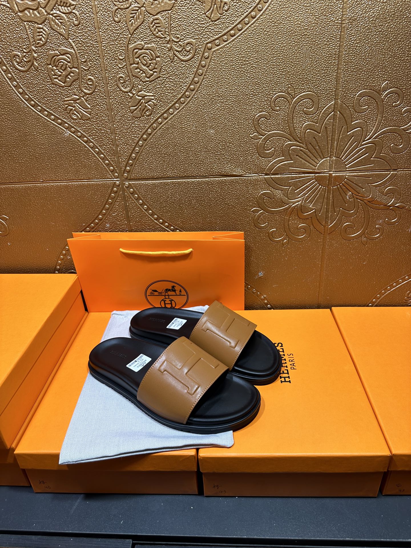 Hermes slide sandals with tan front strap and black sole, pair displayed on box