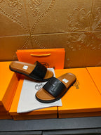 Black leather slide sandals with embossed H strap and tan footbed