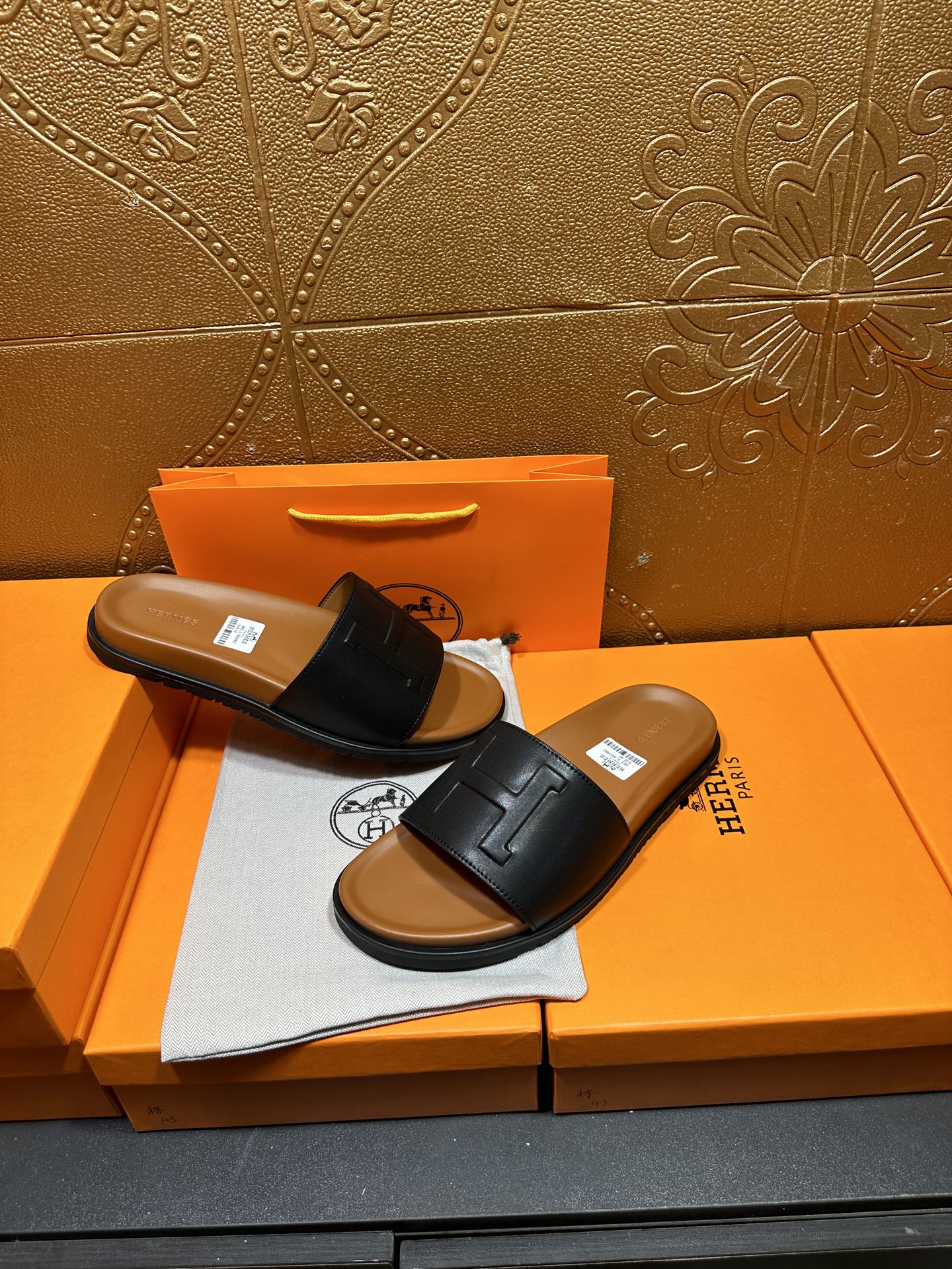 Black leather slide sandals with embossed H strap and tan footbed