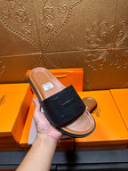 Black leather slide sandal with embossed H strap, tan footbed
