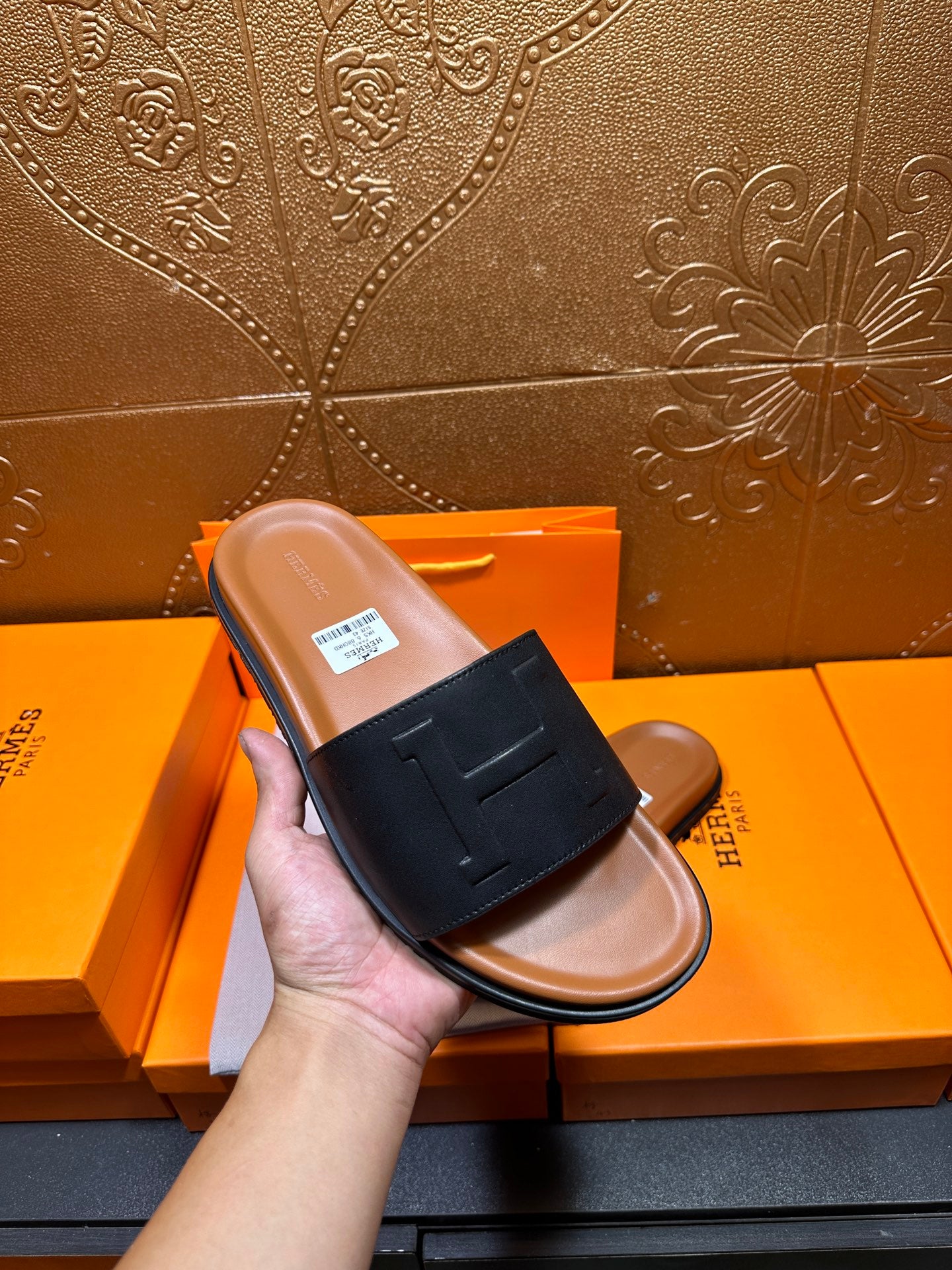 Black leather slide sandal with embossed H strap, tan footbed