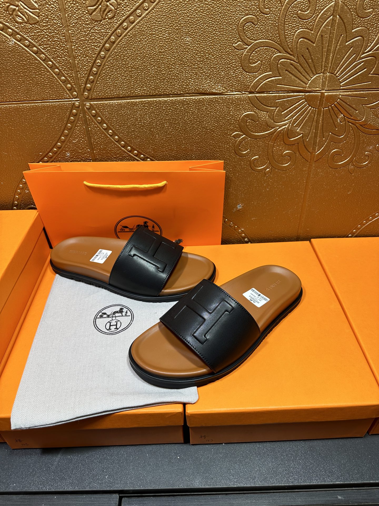 Black leather slide sandals with embossed H strap and tan footbed