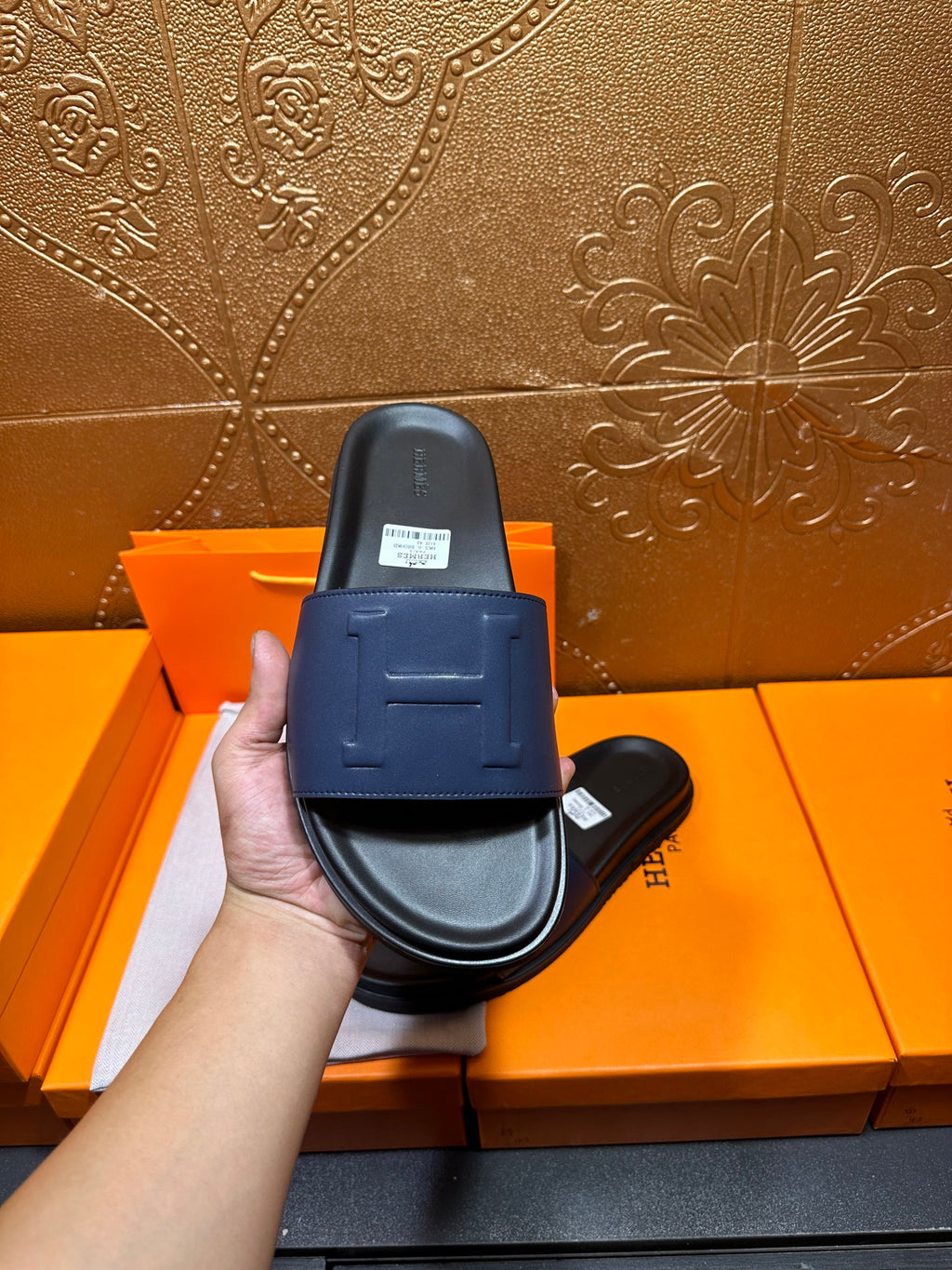 Single leather slide sandal held in hand, wide strap with stitched H detail