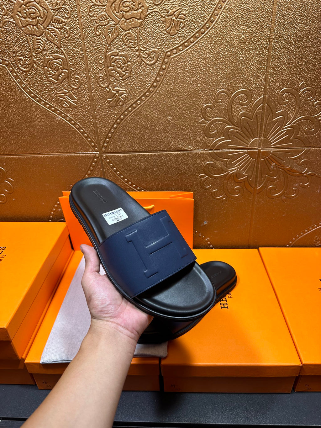 Hand holding a leather slide sandal with wide strap and H stitch detail