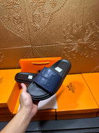 Hand holding a leather slide sandal with wide front strap and H detail