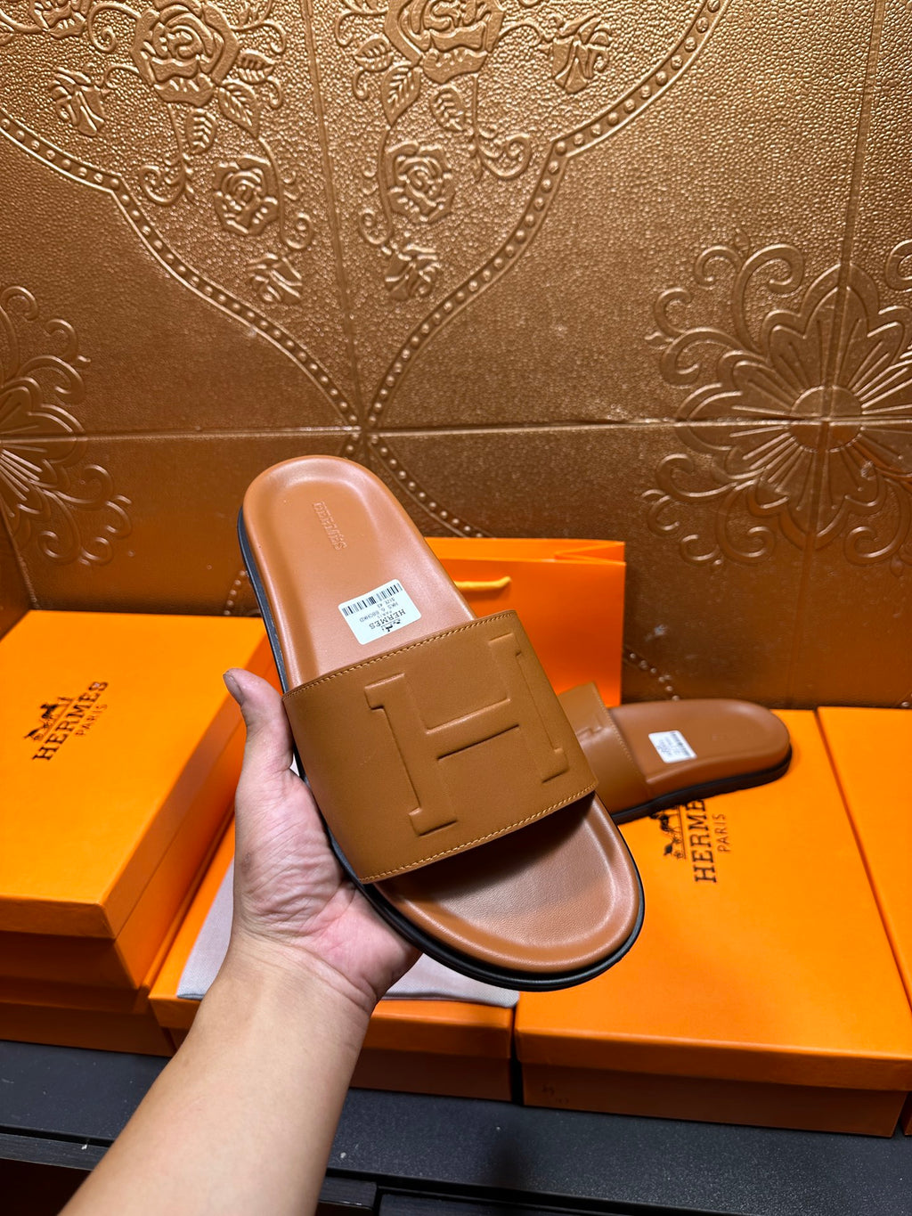Hand holding tan leather Hermes slide sandal with square buckle strap