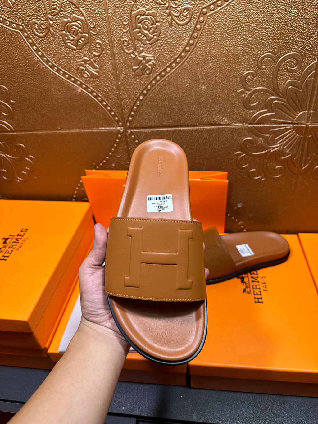 Tan leather Hermes slide sandal held up, featuring square buckle strap