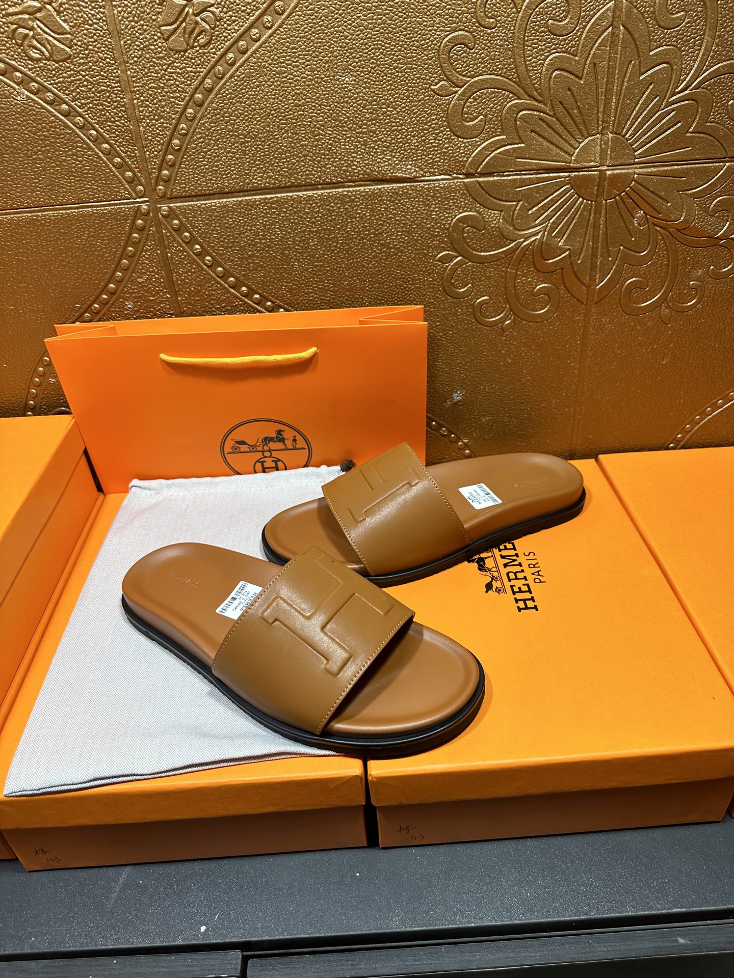Tan leather Hermes slide sandals with square buckle strap, pair angled on box