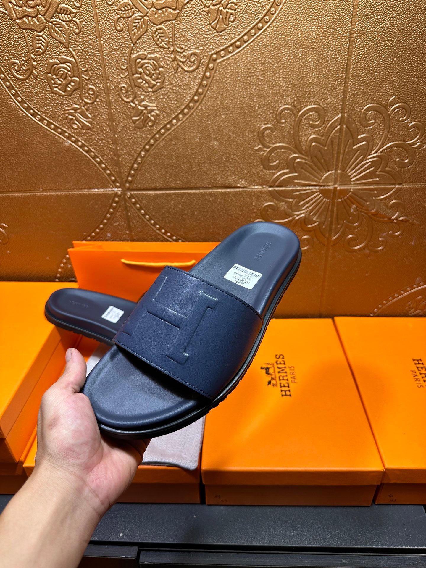 Hermes navy slide sandal held by hand, embossed H front strap