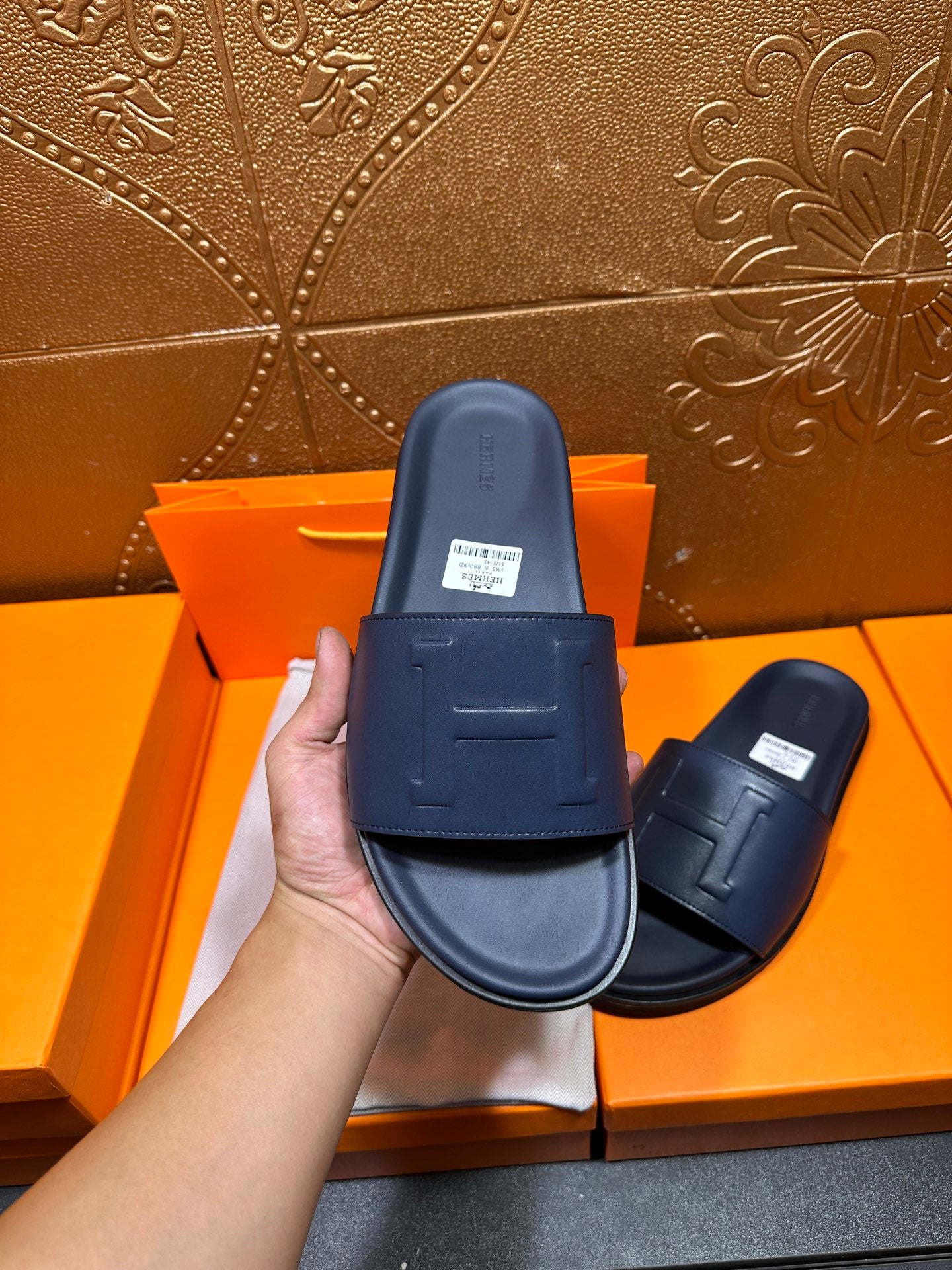 Hermes navy slide sandal held up, wide strap with embossed H and cushioned base