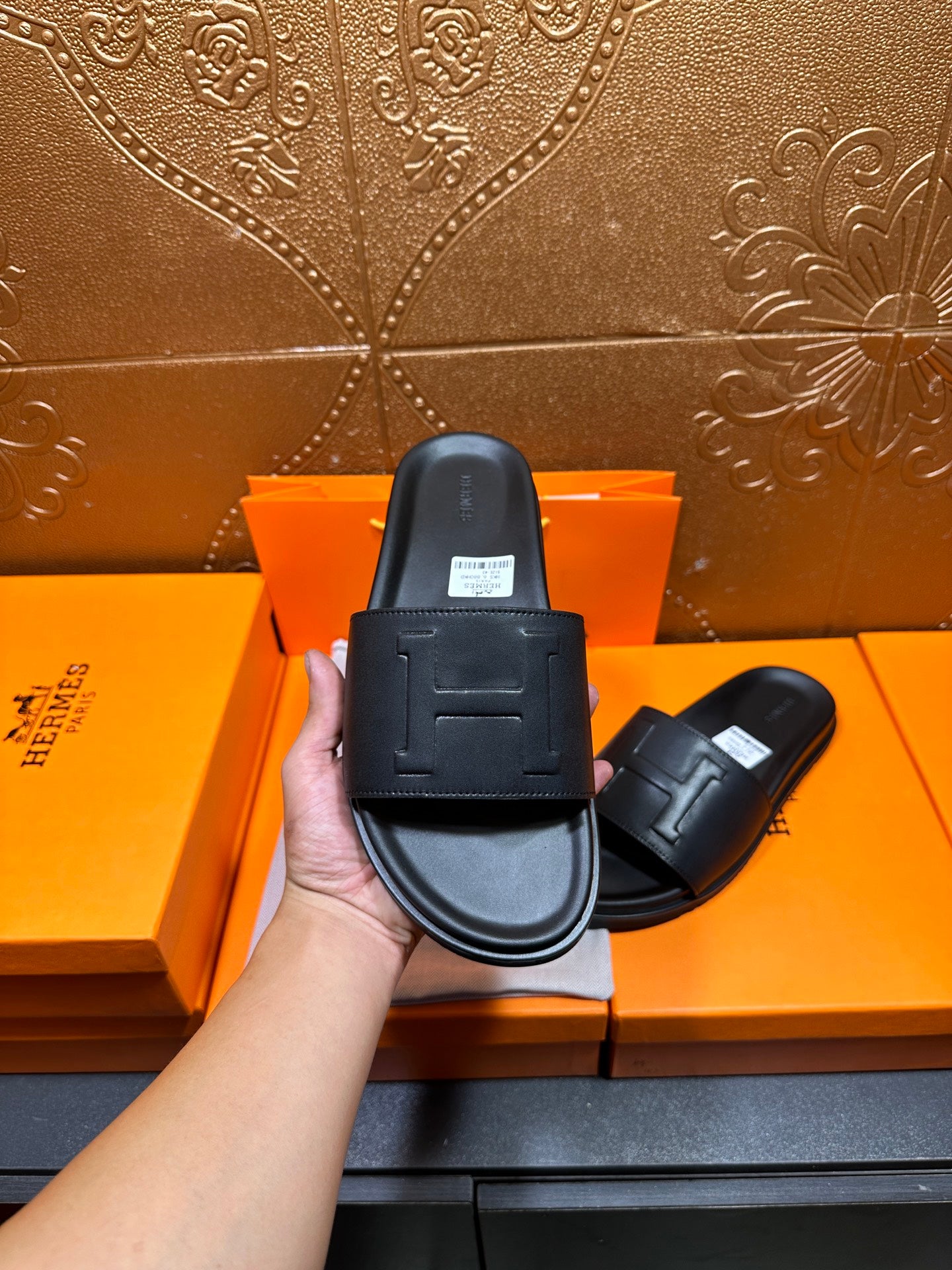 Black Hermes slide sandals in hand, H-style strap detail on one shoe.
