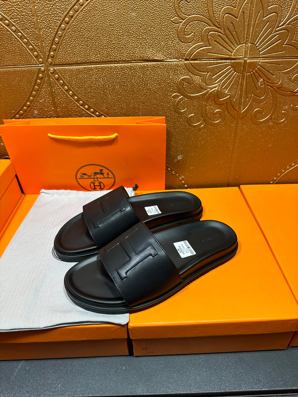 Black Hermes slide sandals with wide strap and H-style logo, pair on display.