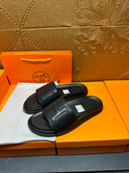 Black Hermes slide sandals with wide strap and H-style logo, pair on display.