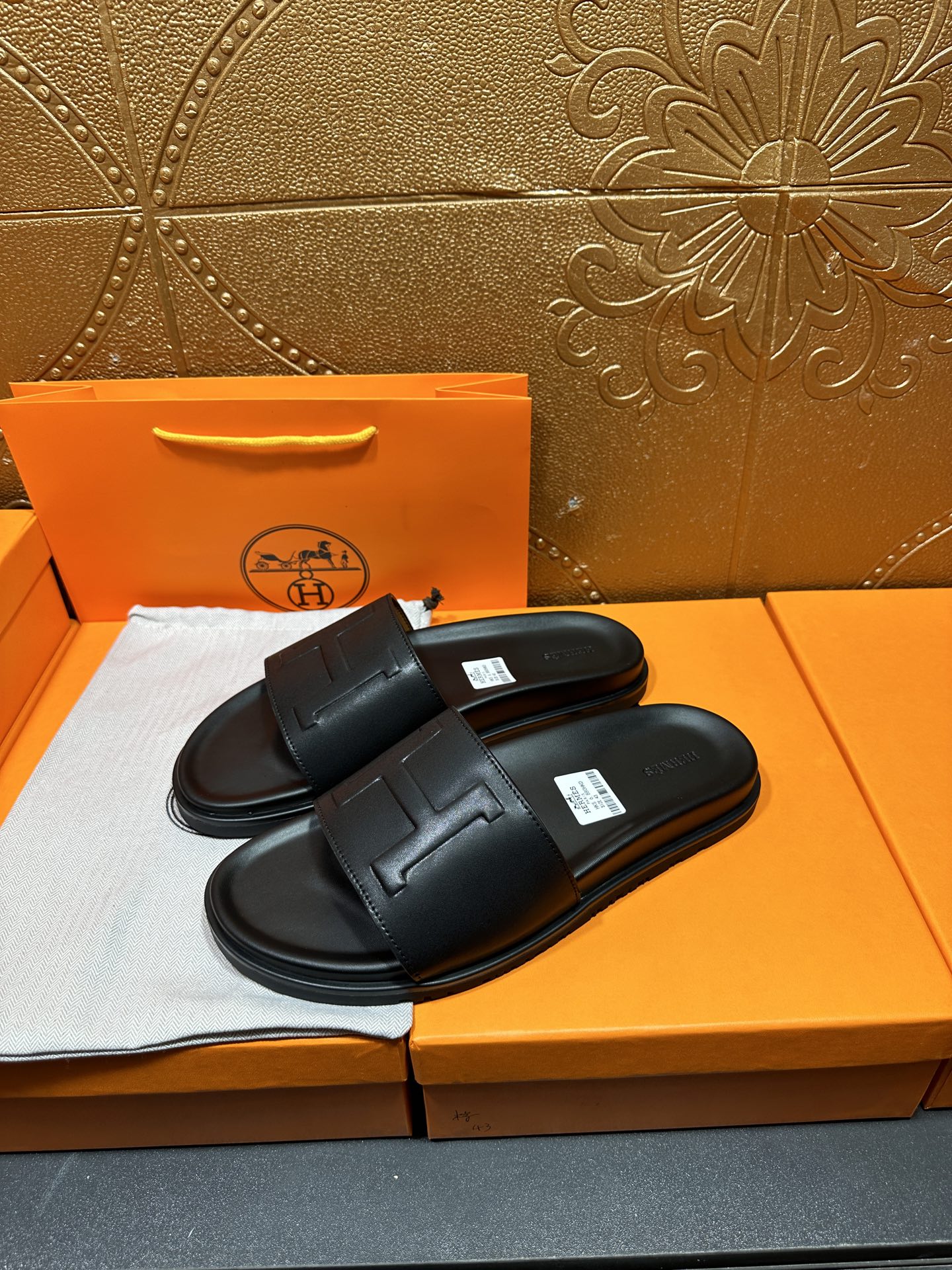 Black Hermes slide sandals with wide strap and H-style logo, pair on display.