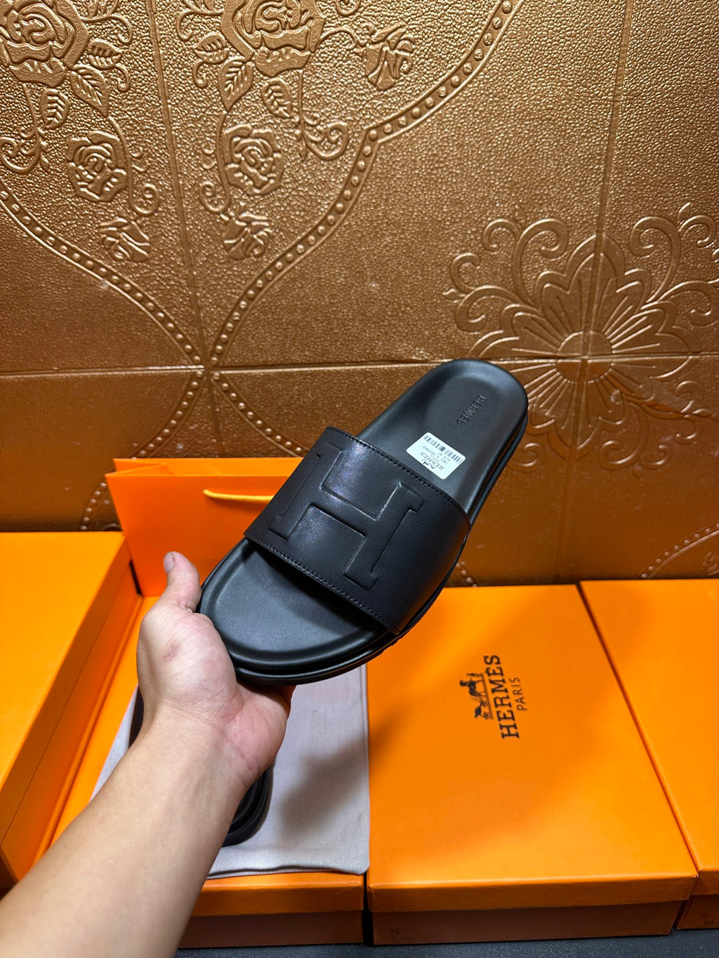 Black Hermes slide sandal held up, wide strap with H-style logo detail.