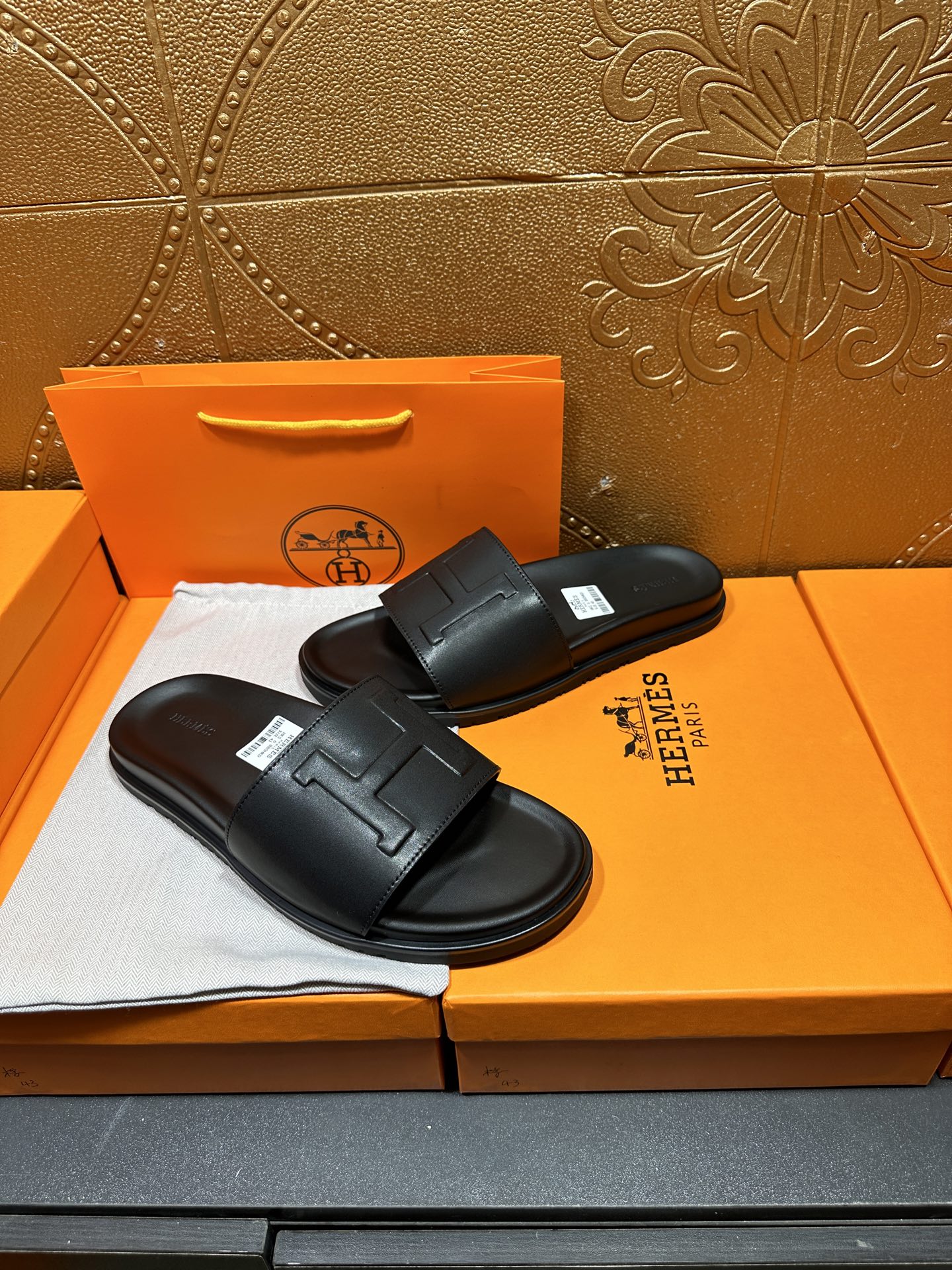 Black Hermes slide sandals with wide straps and H-style logo, pair on box.