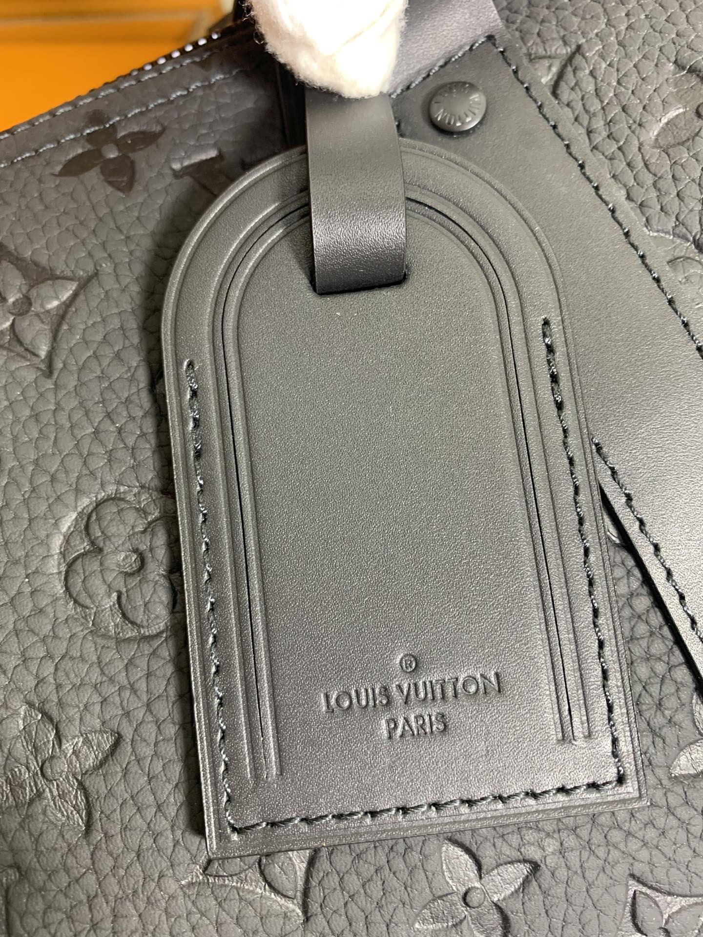 Grained leather luggage tag on monogram duffel bag with debossed logo