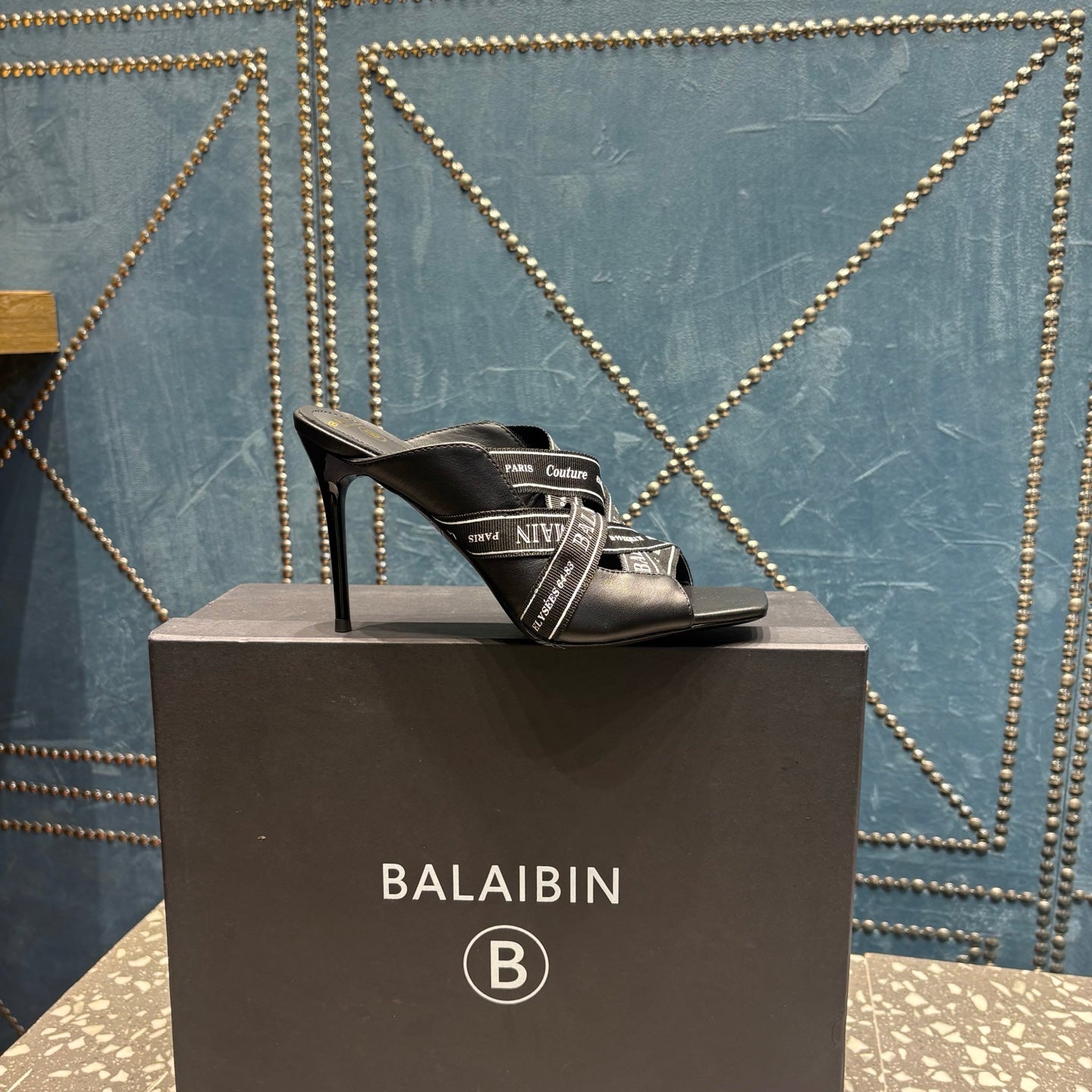 Black mule sandals with open toe and logo-print strap on a pedestal