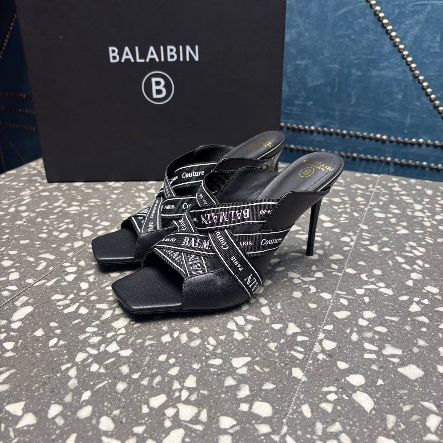 Black open-toe slide sandals with logo-print strap across the foot, stiletto heel
