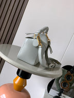 Light blue leather shoulder bag with braided handle, tassel pull, and gold hardware