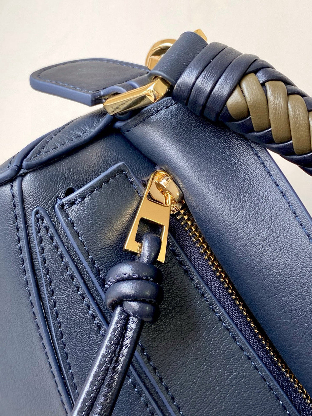 Blue leather bag corner with braided strap and gold zipper pull detail