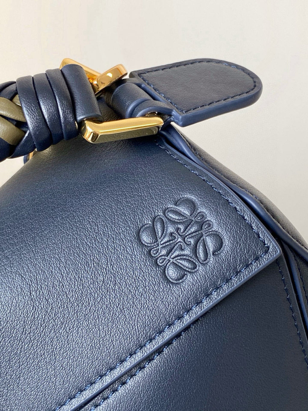 Blue leather handbag front with embossed floral logo on a stitched patch.