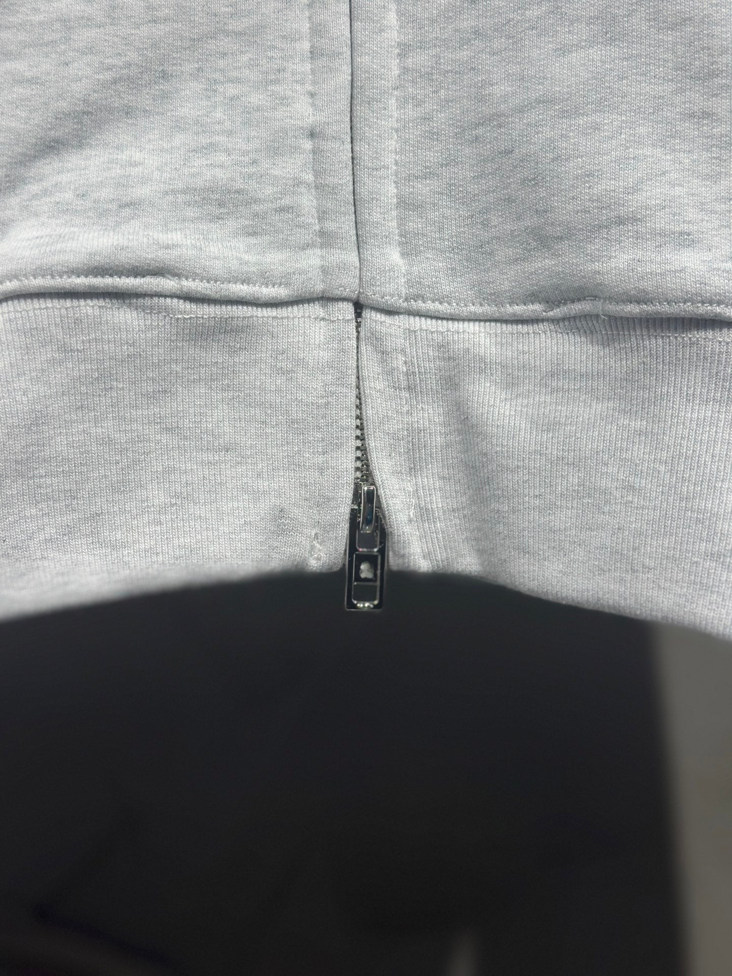 Light gray hoodie front zipper close-up at chest with stitched seam