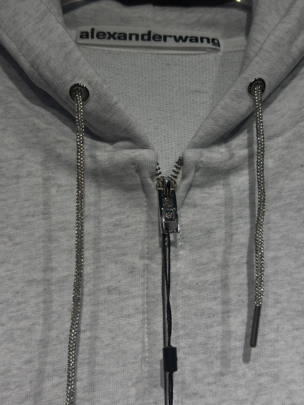 Light gray hoodie close-up with front zipper and dark zipper pulls on drawstring