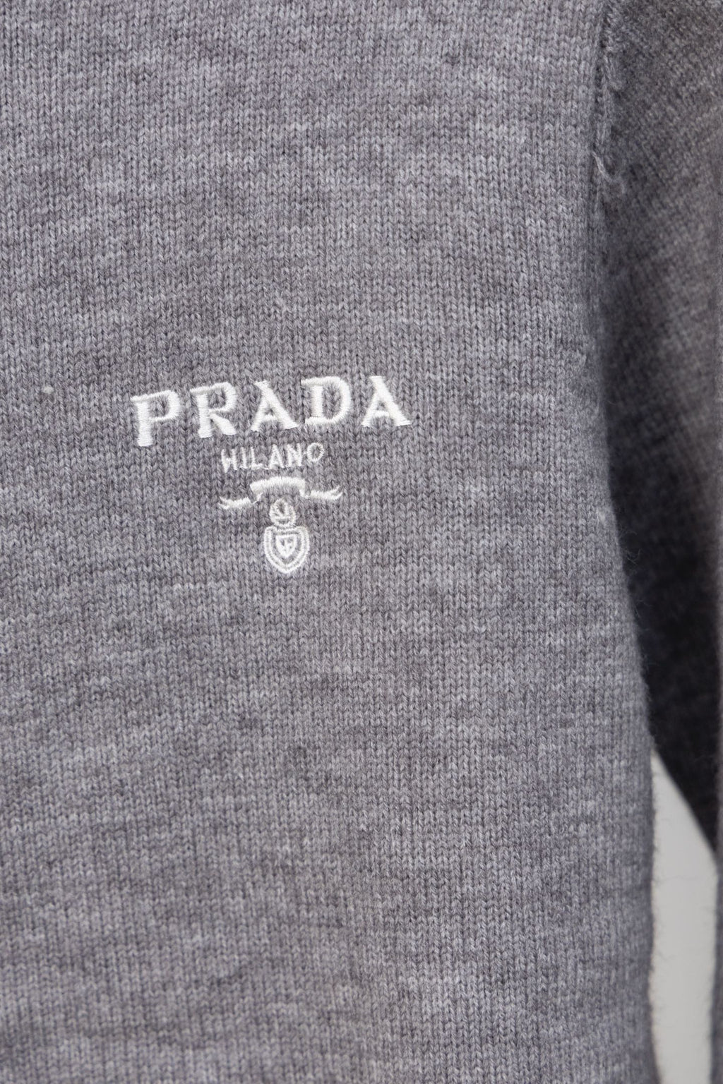 Gray Prada knit sweater chest close-up with PRADA MILANO logo and crest