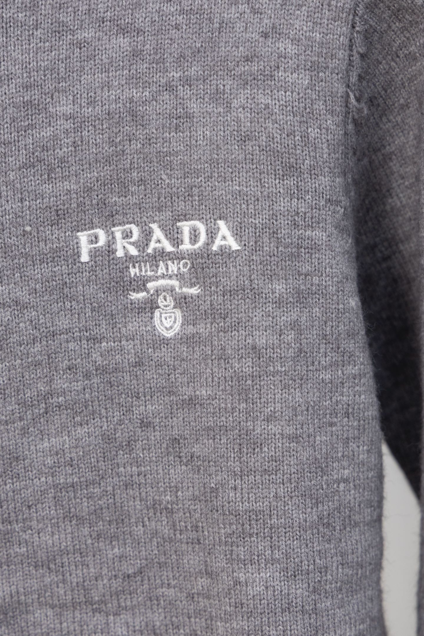 Gray Prada knit sweater chest close-up with PRADA MILANO logo and crest