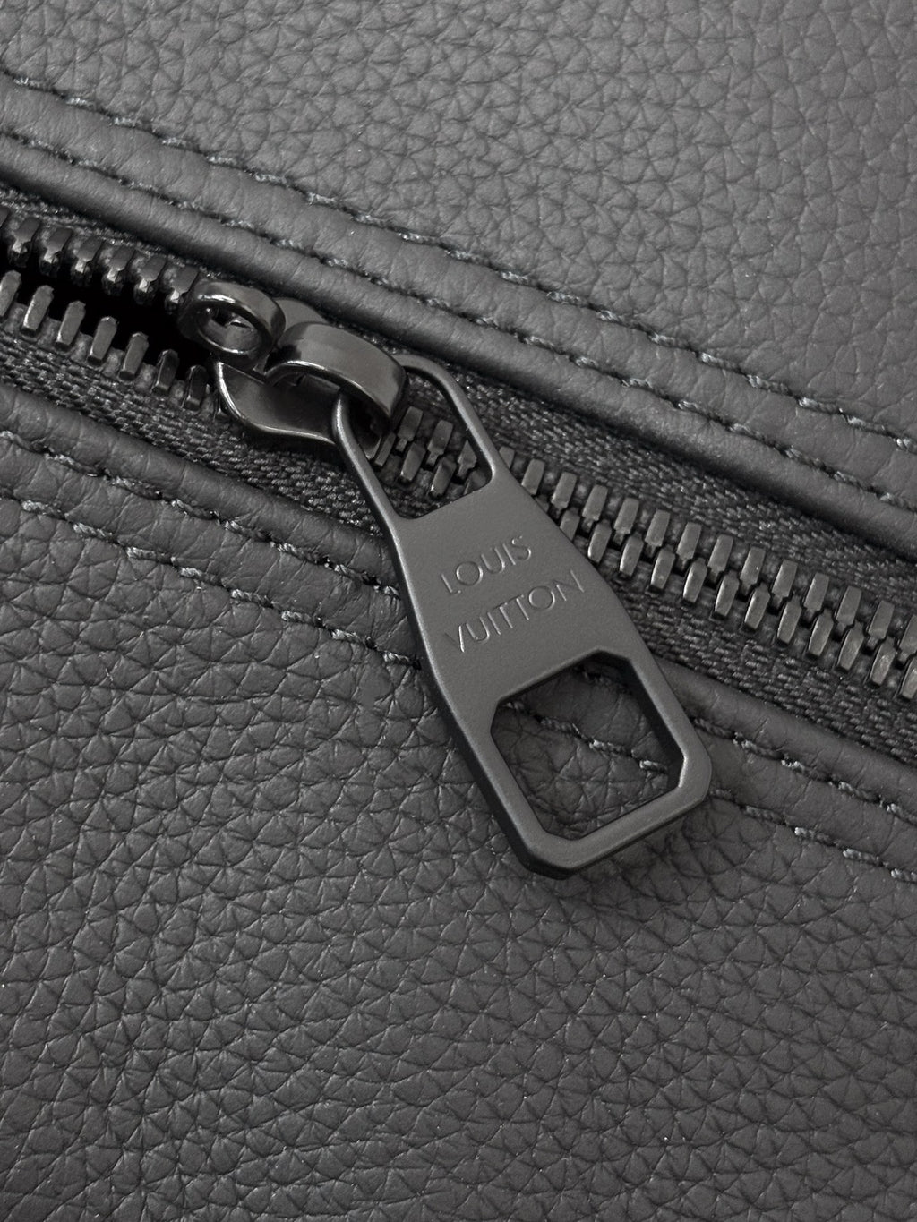 Louis Vuitton bag zipper close-up with metal pull and brand engraving on dark leather.