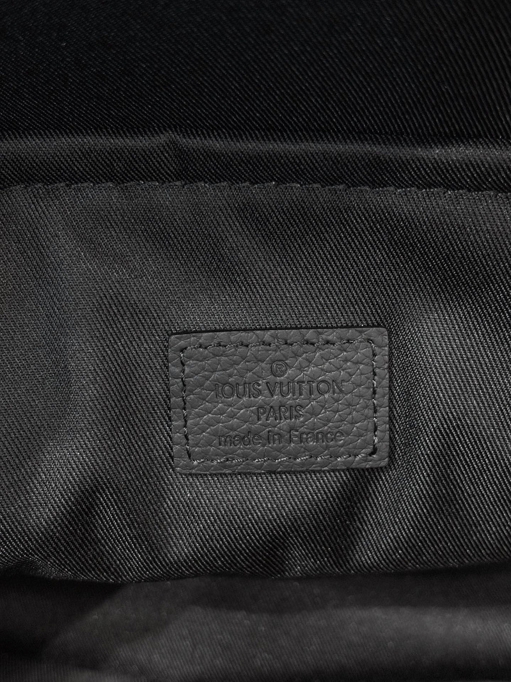 Louis Vuitton bag interior label stitched on dark fabric lining near zipper.