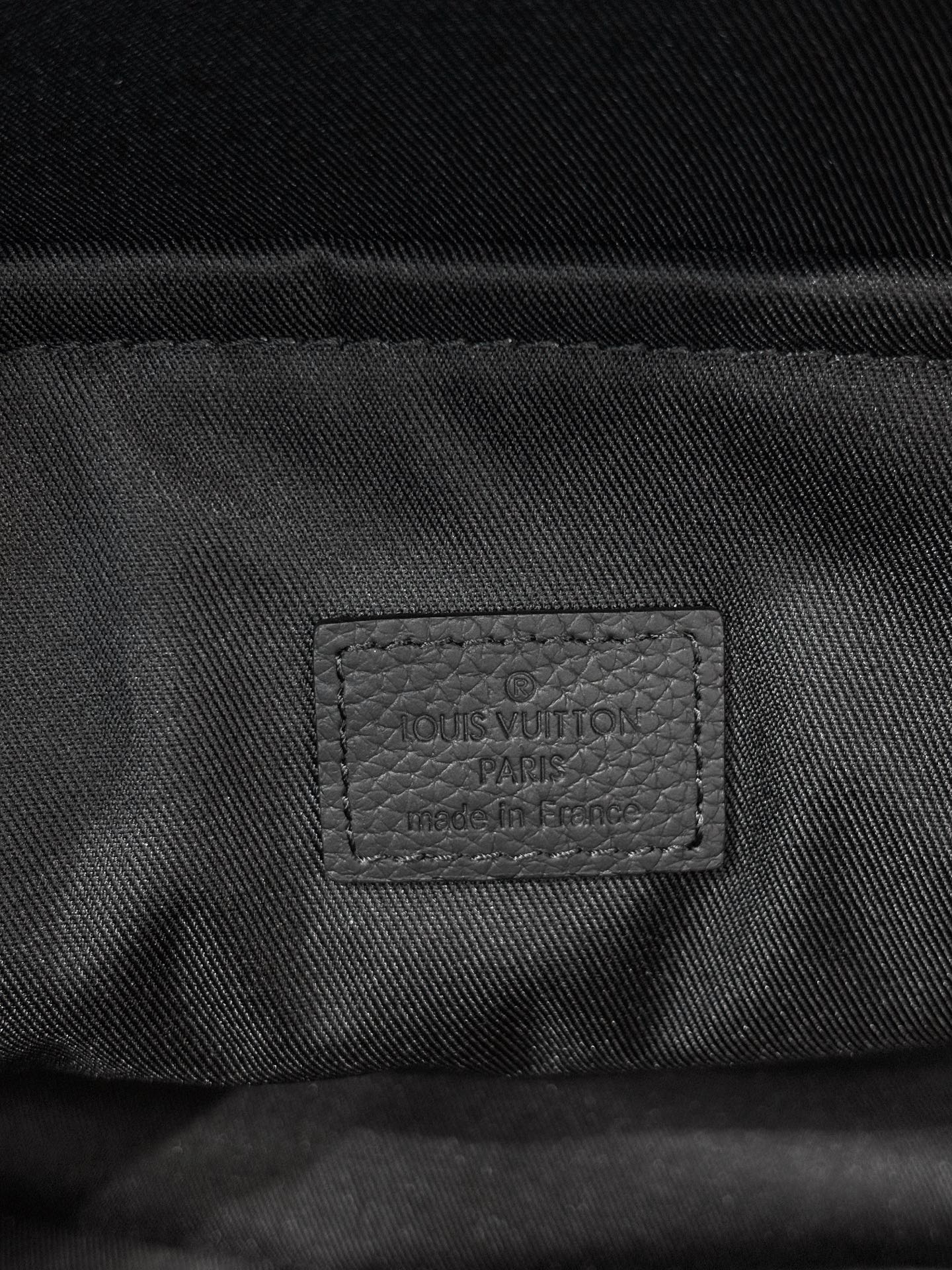Louis Vuitton bag interior label stitched on dark fabric lining near zipper.
