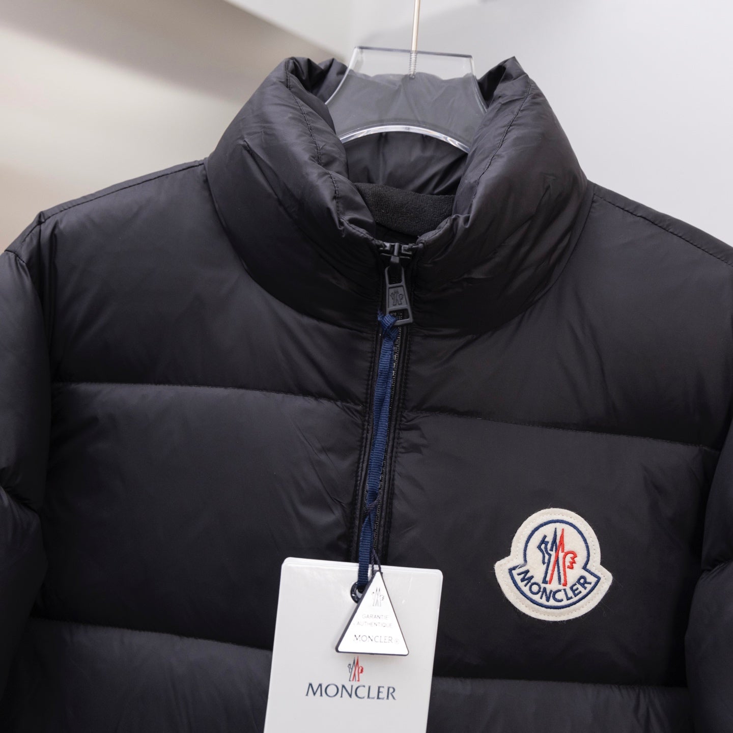 Dark long puffer jacket with front zipper and circular logo patch on chest