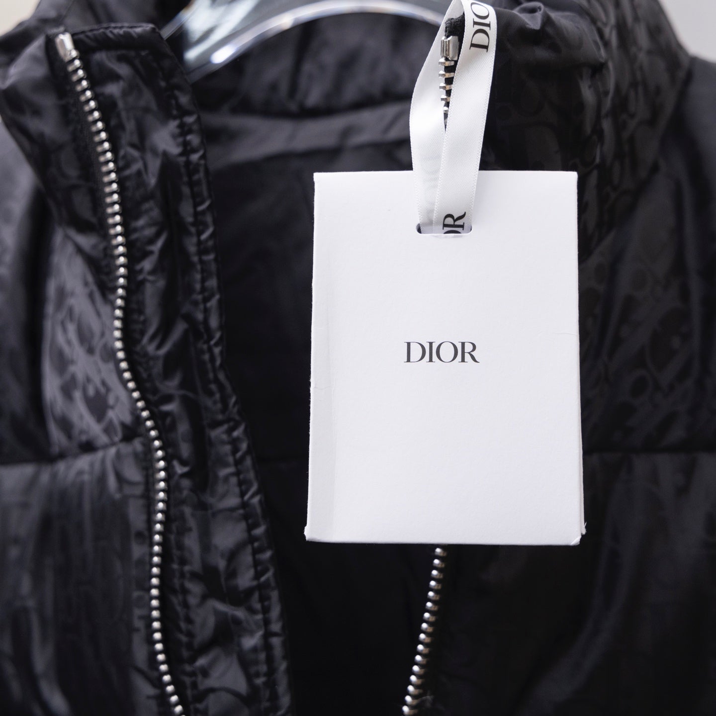 Black Dior puffer jacket with zipper and hanging Dior retail tag.