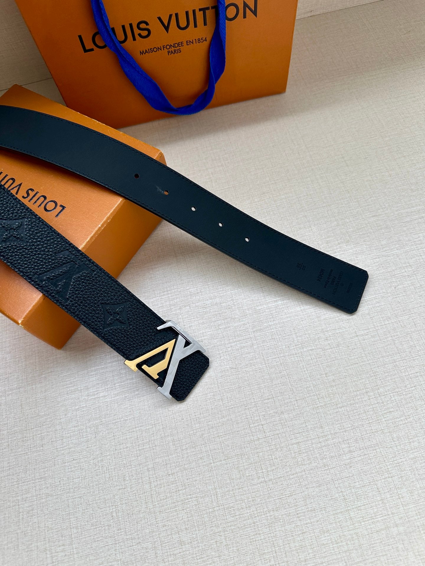 Louis Vuitton belt with dark blue strap and silver LV buckle, laid out