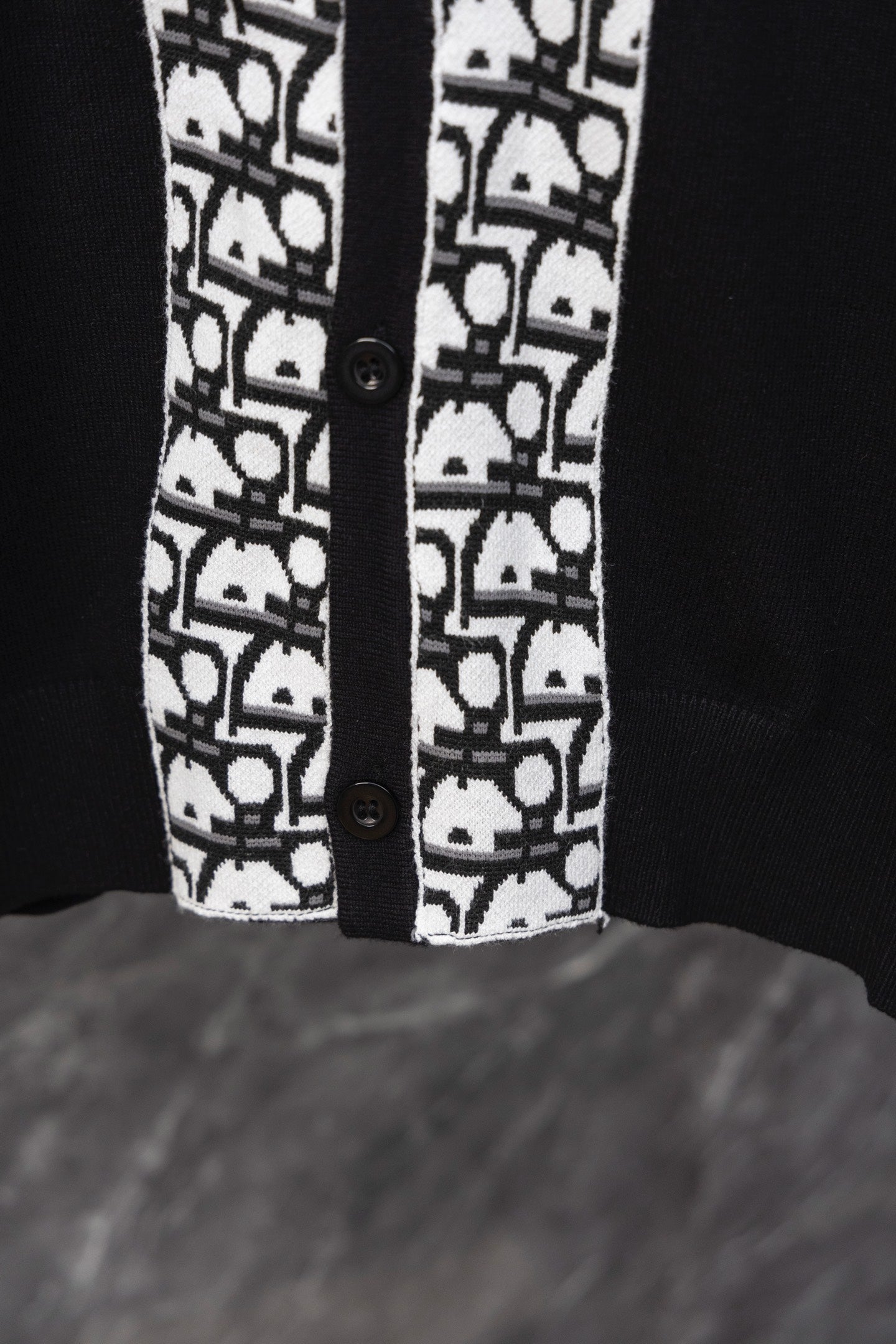 Black cardigan front hem with white patterned trim and two button closures